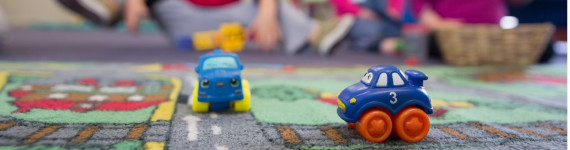 Zwei Spielzeugautos mit mehreren spielenden Kindern im Hintergrund