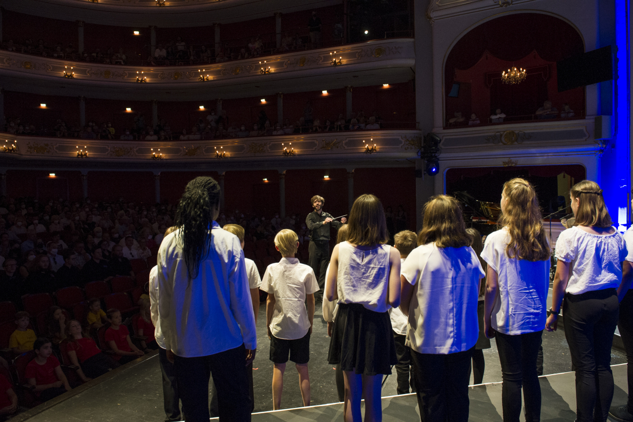 Blick auf den Maxichor von hinten und die Ränge des Opernhauses im Hintergrund.