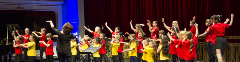 Kinder in roten und gelben Tshirts stehen auf der Bühne und tanzen.