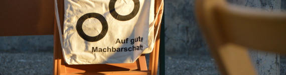Ein Turnbeutel mit der Auschrift "Auf gute Machbarschaft" hängt auf einer Stuhllehne