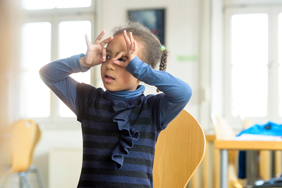 Mäddchen schaut durch ihren Fingern vor das Gesicht