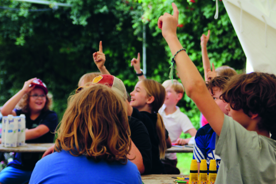 Viele Kinder am Tisch melden sich, um eine Frage zu beantworten