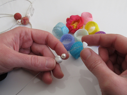 Foto von 2 Händen. Die Hände halten einen Schmuck·draht. Die Person fädelt gerade Perlen auf den Schmuck·draht., Bild © Erfahrungsfeld / Stadt Nürnberg