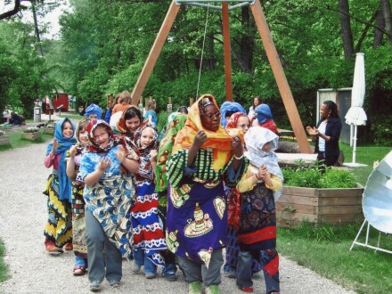 Foto von vielen Kindern in afrikanischen Kostümen. Die Kinder laufen einen Weg entlang. Vorne läuft eine erwachsene Frau mit einem afrikanischen Kostüm., Bild © Erfahrungsfeld / Stadt Nürnberg