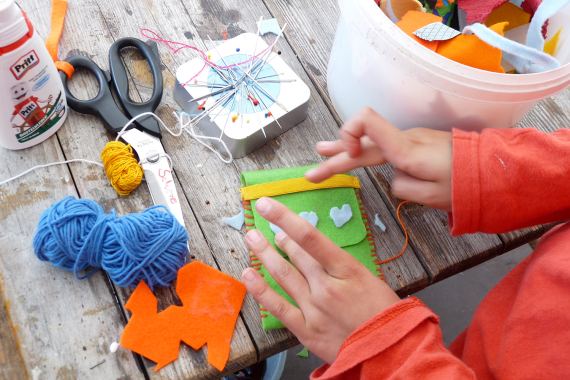 Aus Schere, Nadel und Faden bastelt ein Kind eine Handytasche