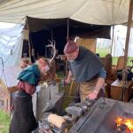 Ein Kind schmiedet gemeinsam mit einem Schmied ein kleines Stück glühendes Eisen am Amboss.