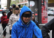 Ein junge mit Augenbinde geht durch die Straße. Ihm folgen weitere Kinder.