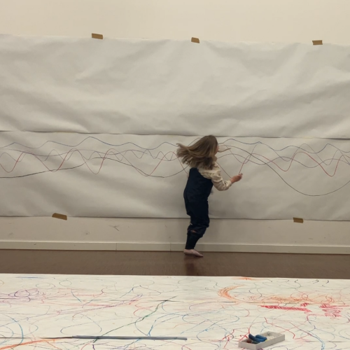 Kind malt mit Wachsmalkreide auf Papierbahn auf Wand