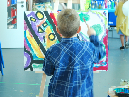 Foto von einem Kind beim Malen. Das Kind malt mit einem Pinsel auf eine Leinwand., Bild © KinderKunstRaum / Stadt Nürnberg