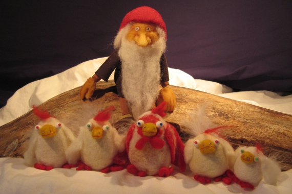 Der Wichtel Tomte trägt eine rote Zipfelmütze und sitzt mit fünf Hühnern in einer Schneelandschaft.
