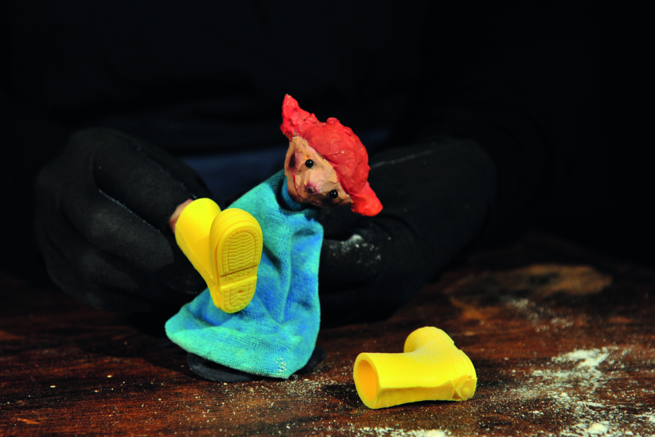Eine kleine rothaarige Figur im blauen Kleid hat zwei quietschgelbe Gummistiefel gefunden., Bild © Anita Pinggera / Figurentheater unterwegs