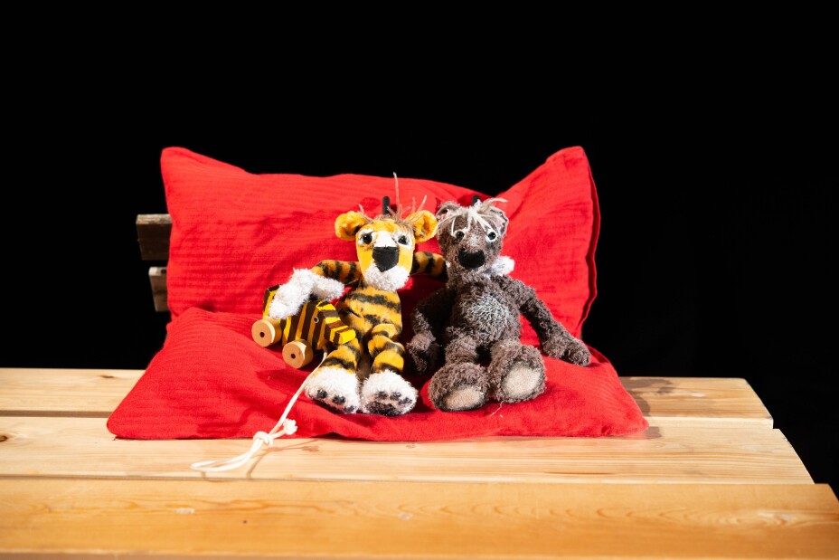 Tiger und Bär sitzen Arm in Arm auf einem großen roten Kissen. T, Bild © Christine Basler / Figurentheater Hattenkofer