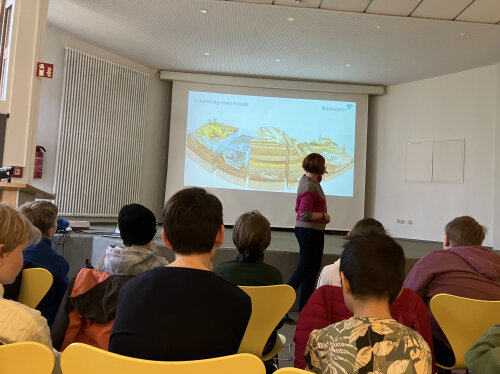 Frau steht vor einer Präsentation zum Thema Evolution. Kindervon hinten schauen zu.