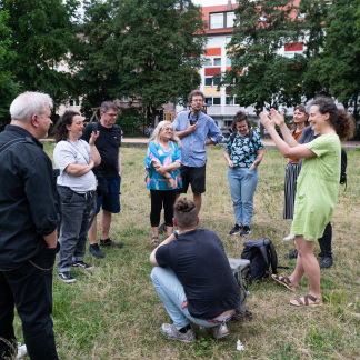 ( Bild: Oleksandra Shyshlakova / Stadt Nürnberg ) Mehrere Personen auf einer Wiese stehen im Kreis und reden miteinander