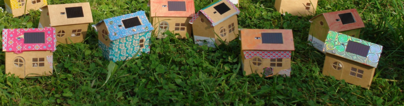 Kleine bunt bemalte udn beklebte Häuser aus Pappe mit kleinen Solarzellmodulen stehen in einer grünen Wiese., Bild © N-Ergie Aktiengesellschaft und Cri-Cri-Events