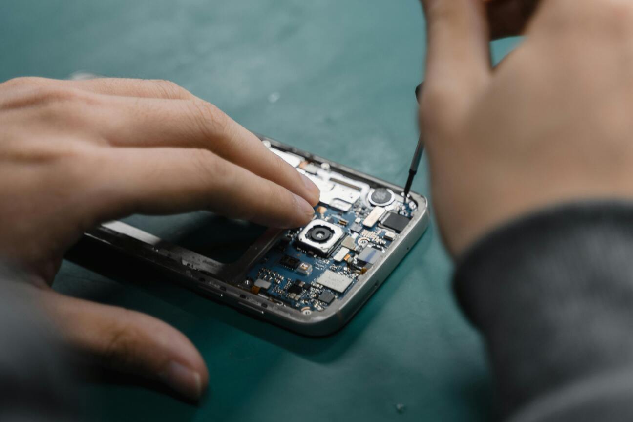 Nahaufnahme von Händen, die mit einem Schraubendreher die Elektronik eines geöffneten Smartphones reparieren.