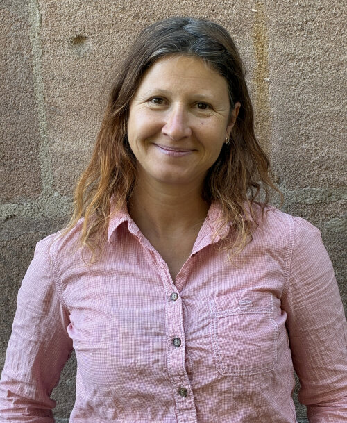 © Kulturladen Röthenbach / Stadt Nürnberg Eine Frau mit braunen, schulterlangen, lockigen Haaren steht vor einer Sandsteinwand und lächelt. Sie trägt eine rosa Bluse. © Kulturladen Röthenbach / Stadt Nürnberg