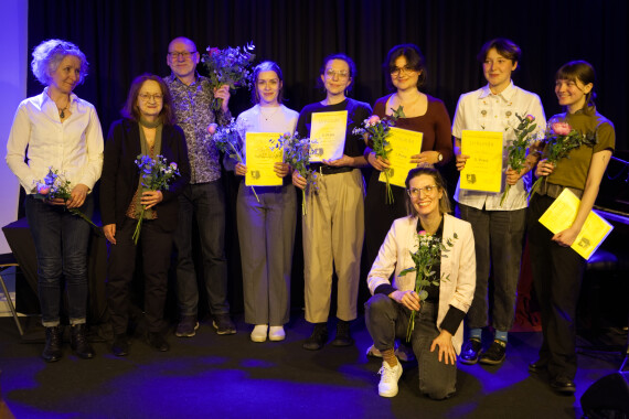 Fünf junge Frauen mit Urkunden stehen zusammen mit vier weiteren Personen auf einer Bühne im blauen Scheinwerferlicht