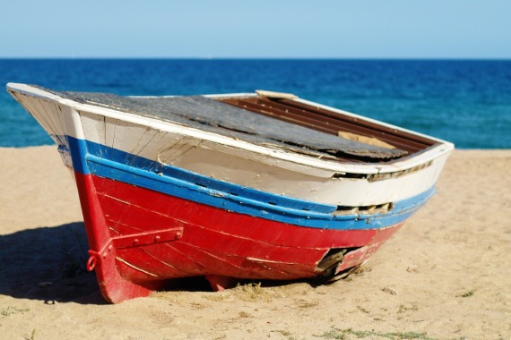 Ein weiß-blau-rot-gestreiftes Holzboot liegt am Strand