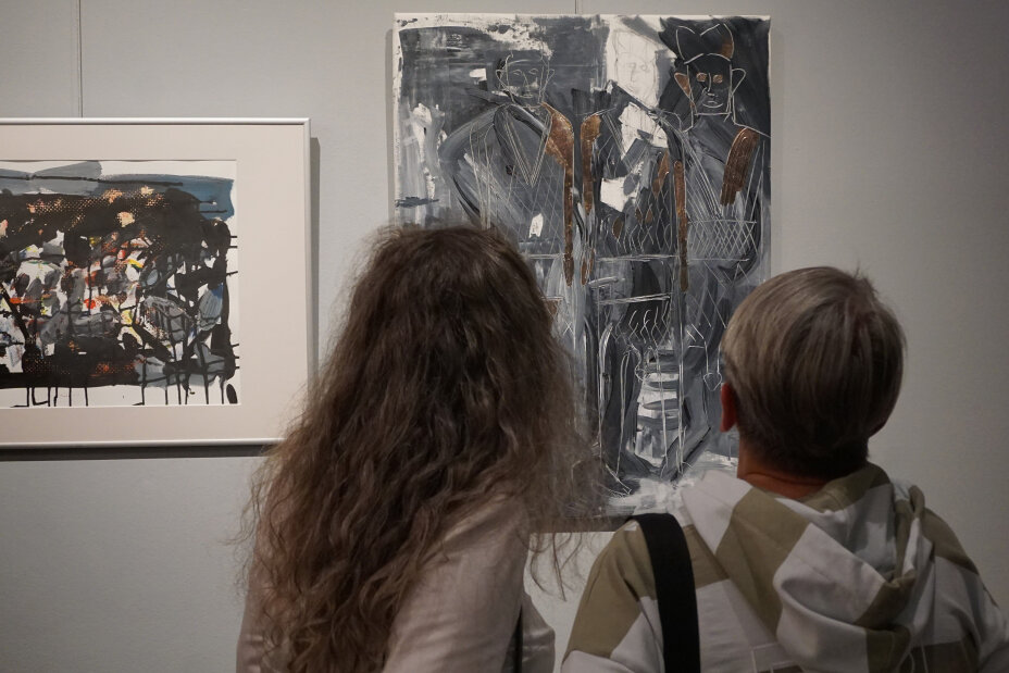 Zwei Frauen begutachten die Kunst. Vor ihnen hängen zwei Bilder an einer weißen Wand. Es sind abstrakte Gemälde mit grauen, schwarzen Farben und Formen und goldenen Akzenten., Bild © Sonja Wolfstädter / Stadt Nürnberg