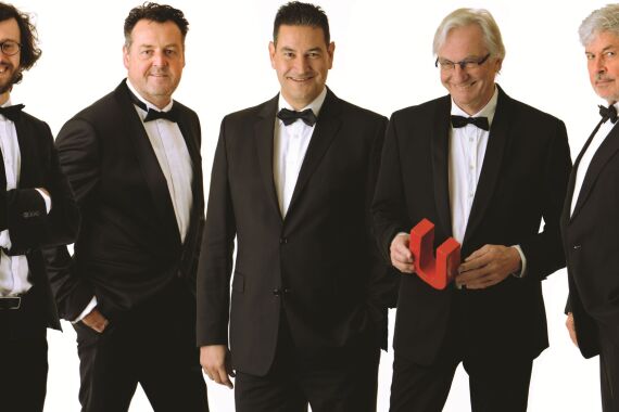 Fünf Männer mit weißen Hemden, Schwarzen Fliegen und schwarzen Anzügen stehen nebeneinander und schauen in die Kamera