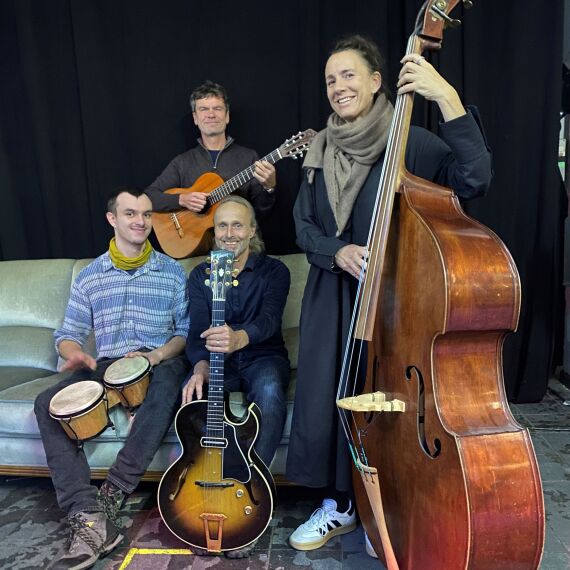 Vierköpfige Musikgruppe posiert mit ihren Instrumenten, einem Kontrabass, zwei Gitarren und Bongos.