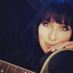 Eine Frau mit langen schwarzen Haaren hält eine Gitarre in der Hand.