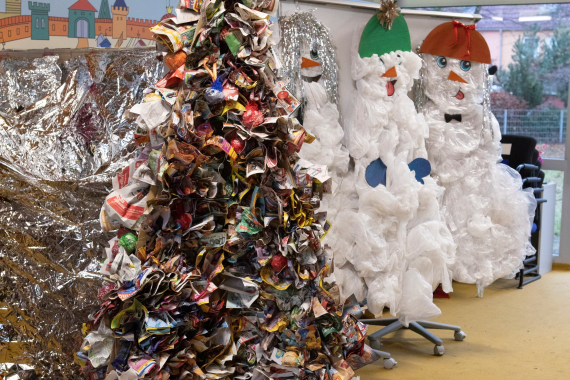 In einer Einganshalle stehen ein Weihnachtsbaum aus Altpapier und zwei Schneemänner aus weißen Plastiktüten