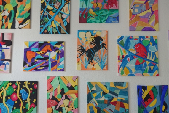 An einer Wand hängen 14 abstrakte Bilder in bunten Farben