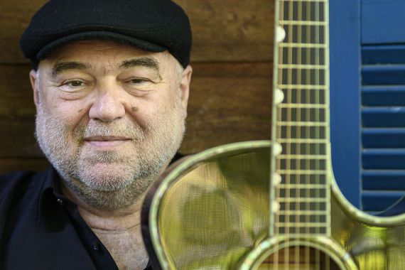 Ein Mann mit schwarzer Kleidung hält eine Gitarre hoch