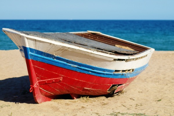 Ein kleine Fischerboot mit weiß-rot-blauer Bemalung liegt am Sandstrand vor blauem Meer.