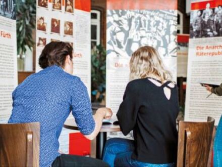 Foto von 2 Personen von hinten. Die Personen sitzen an einem Tisch in einer Ausstellung zu einem politischen Thema., Bild © Andrea Döbler / Villa Leon