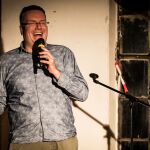 Ein Mann auf der Bühne, mit Mikrofon. Er lacht.