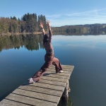 Eine Person auf einem Steg am See in einer gestreckten Yoga-Pose.