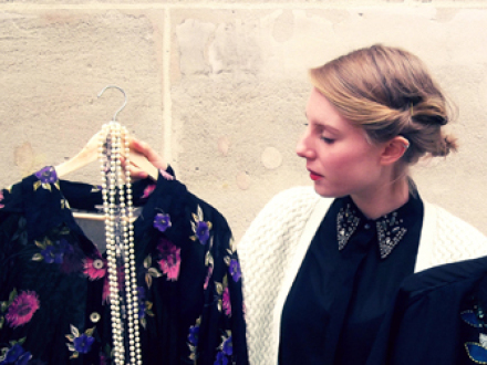 Foto von einer Frau mit einem Kleid in der Hand. Das Kleid hängt auf einem Bügel. An dem Bügel hängt auch eine lange Perlen·kette., Bild © Marlene Molitor / Stadt Nürnberg