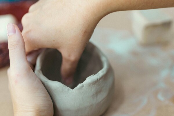 Zwei Hände formen eine runden Behälter aus Ton