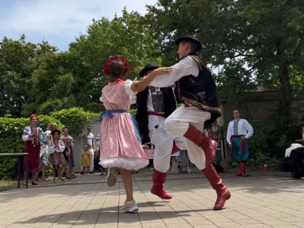 Foto von 3 ukrainische Kinder beim Tanzen. Die Kinder haben traditionelle Kleidung an. Im Hintergrund stehen noch mehr Menschen und schauen zu., Bild © Kulturladen Zeltnerschloss
