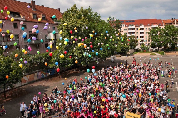 Menschenmenge mit fliegenden Ballons mit Bäumen und Häusern im Hintergrund