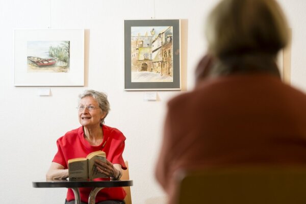 Eine Frau ließt aus einem Buch vor einem kleinen Publikum