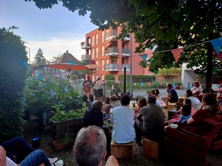 Foto von einem Konzert bei der Veranstaltung Soundgarten. Viele Menschen sitzen in einem Garten und hören den Musikern auf der Bühne zu., Bild © Lena Naumann