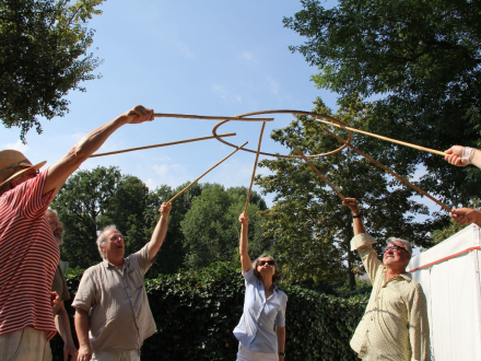 Foto von einer Gruppe von Personen. Die Personen stehen im Kreis. Jede Person hat einen Holz∙stab in der Hand. Mit den Holz∙stäben halten die Personen zusammen einen Holz∙ring in die Höhe., Bild © Stadt Nürnberg