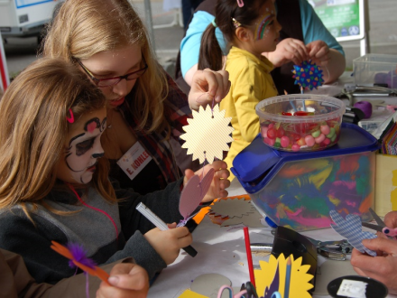 Foto von Kindern an einem Tisch. Die Kinder basteln. Ein Kind zeigt einem anderen eine ausgeschnittene Sonne aus gelbem Papier., Bild © Gerhard Gassner