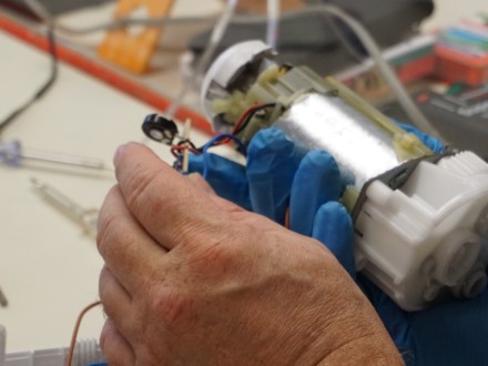 Foto von 2 Händen und einem kaputten Teil von einem technischen Gerät. Das kaputte Teil wird repariert., Bild © Svenja Holy