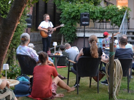 Menschen sitzen im Gras und auf Stühlen und hören einem Musiker mit Gitarre zu., Bild © Kulturladen Ziegelstein