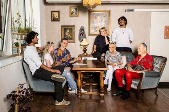 Foto von einer Gruppe von Menschen. Die Menschen in der Gruppe sind sehr unterschiedlich. Es gibt alte Menschen. Es gibt junge Menschen. Es gibt Menschen mit heller Haut. Es gibt Menschen mit dunkler Haut. Es gibt Frauen. Und es gibt Männer. Die Menschen sitzen um einen Tisch und unterhalten sich.