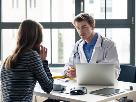 Das Bild zeigt einen Arzt und eine junge Patientin. Der Arzt und die Patientin sprechen miteinander. Das Gespräch ist vertraulich.