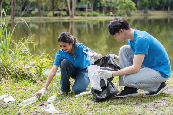 Foto von einer jungen Frau und einem jungen Mann arbeiten an dem Ufer von einem See. Die beiden sammeln Müll ein.