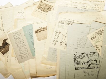 Auf dem Bild sind viele alte Blätter aus Papier. Auf manchen Blättern ist ein Foto oder eine Zeichnung. Auf anderen Blättern steht Text.