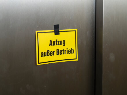 Foto von einem Aufzug mit einem gelben Schild. Auf dem Schild steht: Aufzug außer Betrieb.