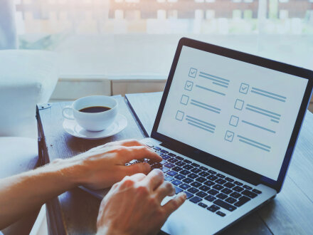 Foto von einem aufgeklappten Laptop auf einem Tisch. 2 Hände tippen etwas auf der Tastatur. Auf dem Bildschirm sieht man eine Umfrage.
